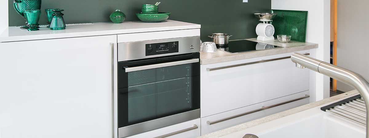 Der moderne Backofen Moderne weiße Küche mit Einbauherd, Induktionskochfeld, Spüle und grünen Glasgefäßen auf der Arbeitsplatte.